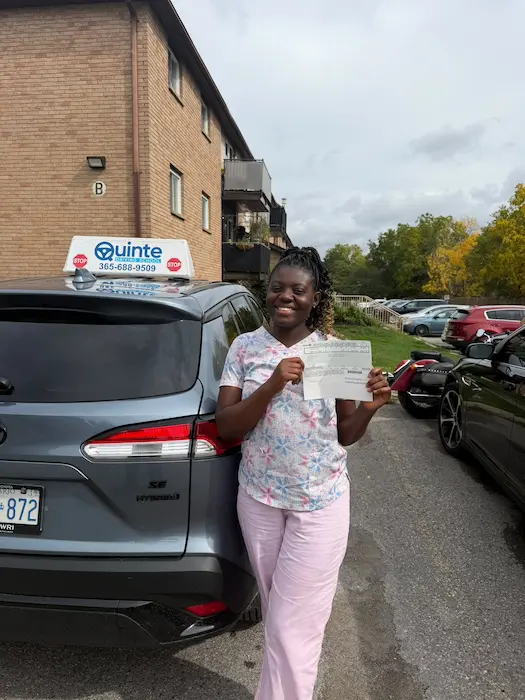 Happy student shows her driving test pass document beside a Quinte Driving School car in Napanee.